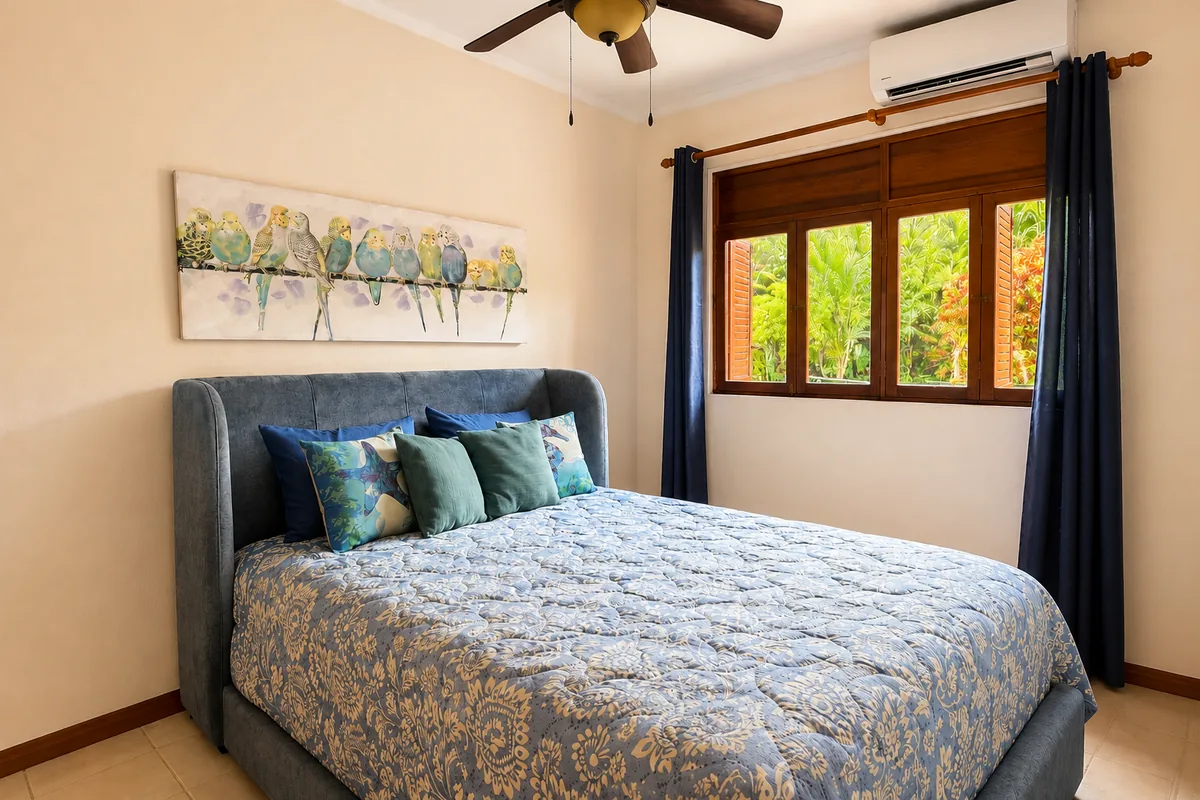 Bedroom with a queen bed in blue upholstery, bird artwork, and a jungle-view window