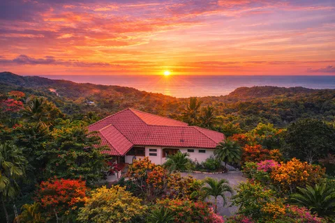 Aerial view of Casa Cascada surrounded by jungle with the Pacific Ocean and a dramatic orange and pink sunset in the background