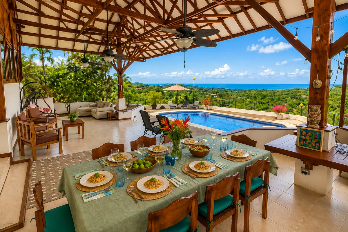 Outdoor dining table set for dinner on the covered terrace, with the pool and Pacific Ocean beyond