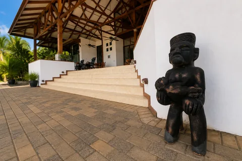 Entrance corner with a carved wooden statue beside the stairs leading up to the covered pavilion