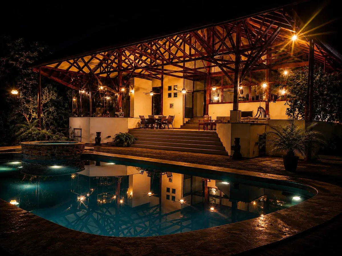 The pool and covered pavilion glowing warmly at night, reflections shimmering across the water