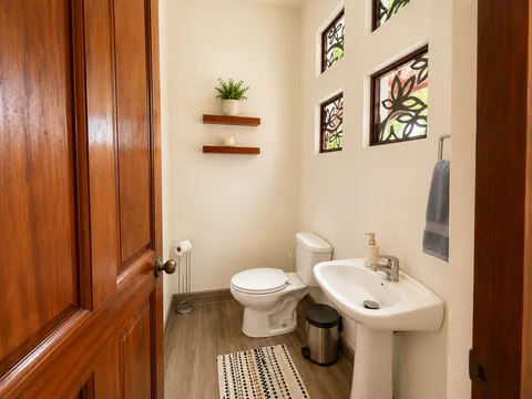 Half-bath in the hallway with a pedestal sink and floral-paned windows