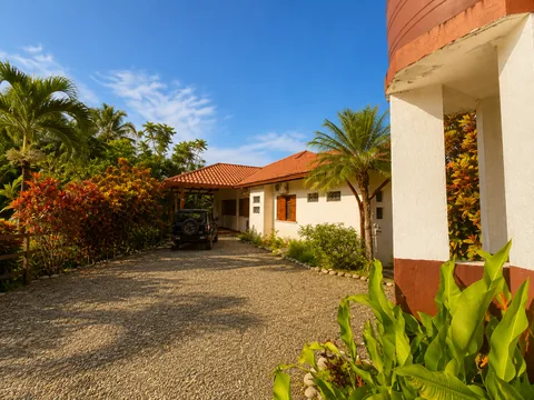 Golden-hour view of Casa Cascada's gravel driveway approach with the tiled-roof villa and tropical landscaping