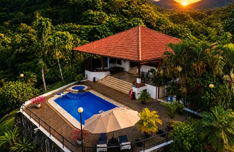 Aerial view of Casa Cascada nestled in the jungle at golden hour, pool and jacuzzi in the foreground with the sun setting between distant mountains